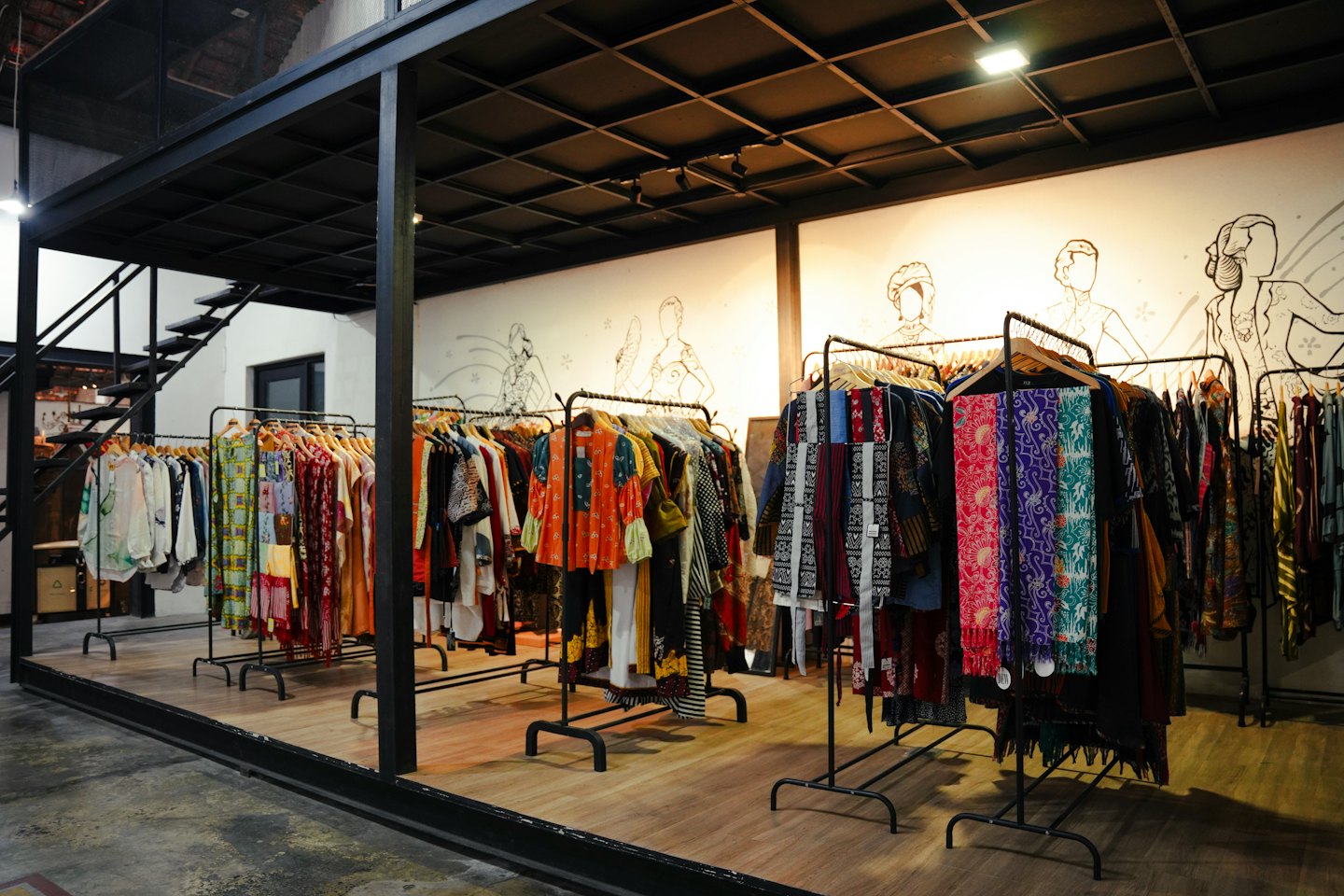 Boutique mit bunten Kleidungsstücken auf Kleiderständern und industriellem Rahmen.